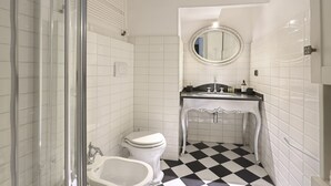 A bathroom with a checkered floor, a toilet, a bidet, a sink with a mirror, and white tiled walls.