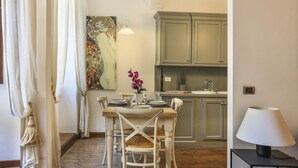 A dining area with a table set for four, a painting on the wall, and a kitchen in the background.
