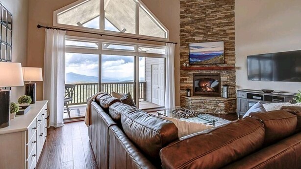 A spacious living room with a large window, a fireplace, and a television. - Updated condo at 5100' with breathtaking views! (Sugar Mountain)