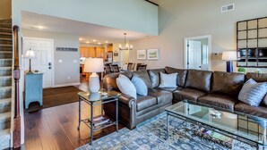 A spacious living room with a leather sofa, a glass coffee table, and a dining area with wooden cabinets and a chandelier. - Updated condo at 5100' with breathtaking views! (Sugar Mountain)