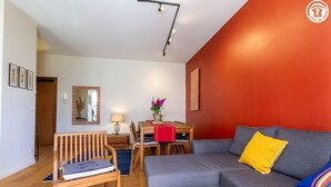Una sala de estar moderna con un sofá gris, sillas de madera, una mesa de comedor con camino de mesa rojo y una pared de acento en rojo.