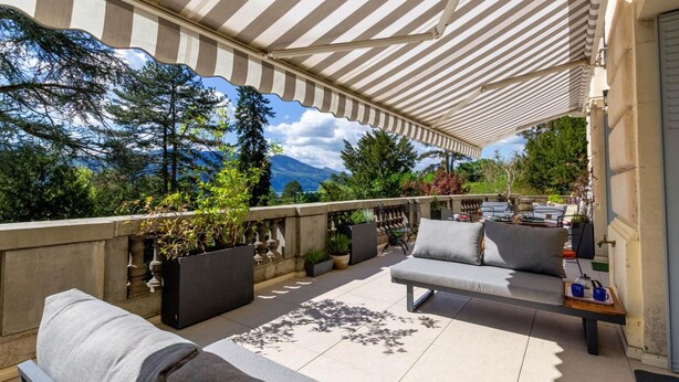 Una terraza al aire libre con un toldo a rayas, un sofá, una mesa con bandeja y plantas en macetas.