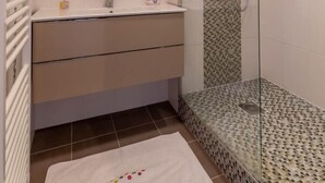 Un baño moderno con ducha envuelta en vidrio, un espejo grande y suelo de baldosas blancas.