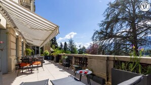 Un patio con mobiliario exterior, una mesa con tazas y vistas a árboles y un edificio.