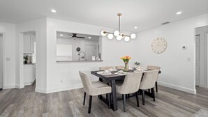 A modern dining area with a dark wooden table, beige upholstered chairs, and a central light fixture.