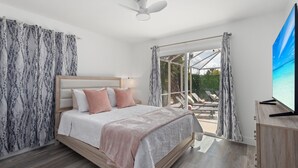 A bedroom with a bed, curtains, a ceiling fan, and a view of an outdoor area with a table and chairs.