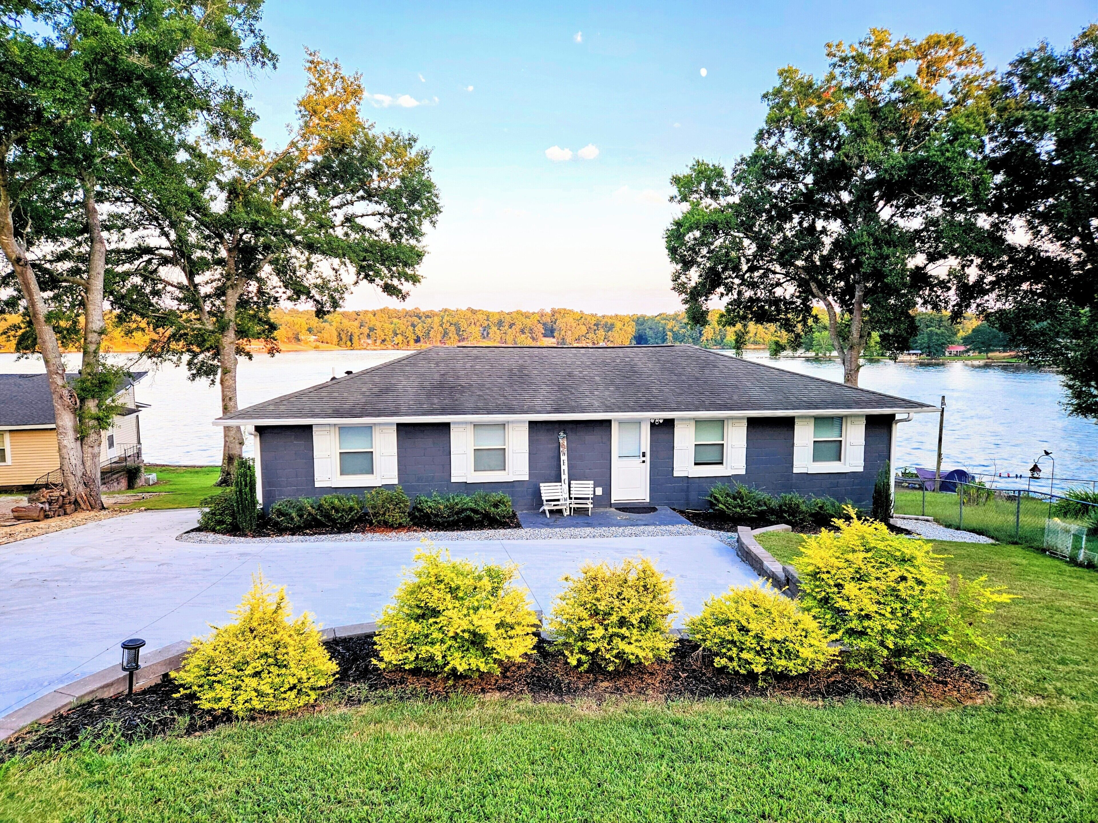 A single-story house with a front porch, a small front yard with bushes, and a view of a lake.
