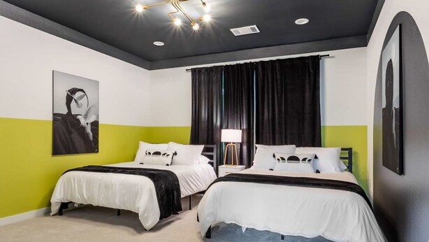 Una habitación de hotel con dos camas, un ventanal con cortinas, una lámpara de techo moderna y obras de arte en las paredes.