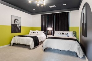 Ein Hotelzimmer mit zwei Betten, einem großen Fenster mit Vorhängen, einer modernen Deckenleuchte und Kunstwerken an den Wänden.