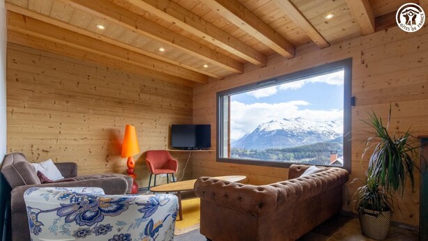 Un interior de madera acogedor con un sofá, un sillón y un televisor montado en la pared.