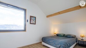 Un dormitorio con un ventanal grande, una cama con ropa de cama estampada, dos lámparas de noche y un cartel enmarcado en la pared.