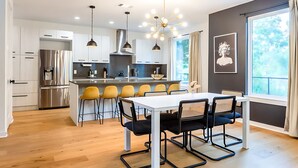 A modern kitchen with a central island, stainless steel appliances, and a dining area with a white table and yellow chairs. - Eastside House Supreme 6 Min Drive to DT (Austin)