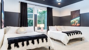 A modern bedroom with two beds, black and white bedding, a large window with curtains, a nightstand with a lamp, and a painting of a space scene. - Eastside House Supreme 6 Min Drive to DT (Austin)