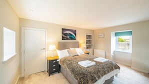 A bedroom with a bed, bedside tables, a window, a door, and a wall-mounted shelf.