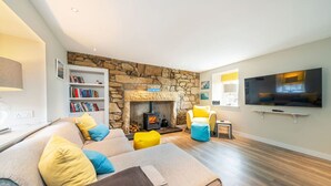 A cozy living room with a stone fireplace, a sofa, a television, and a bookshelf.