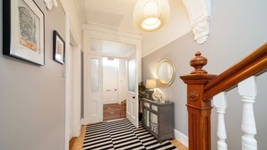 Ein Flur mit einem schwarz-weiß gestreiften Boden, einer Holztreppe mit weißer Wangenverkleidung und einem an der Wand befestigten Spiegel.