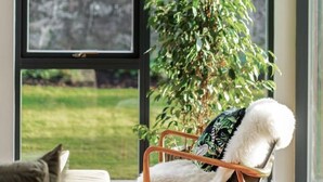 A modern living room with a large window, a wooden chair with a white throw, and a green plant. - Blythewood Holiday Home (Kemnay)