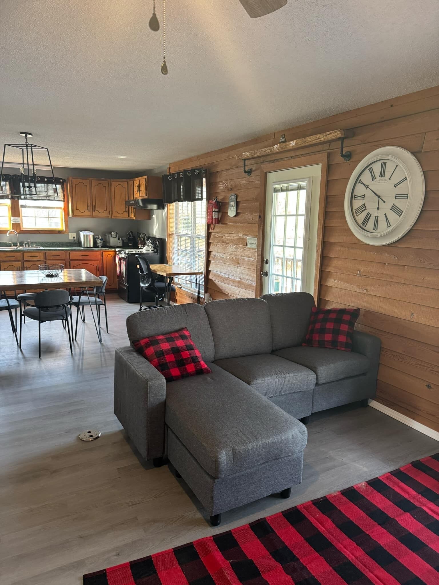 Una sala de estar acogedora con un sofá seccional gris, una mesa de comedor con sillas y una cocina al fondo.