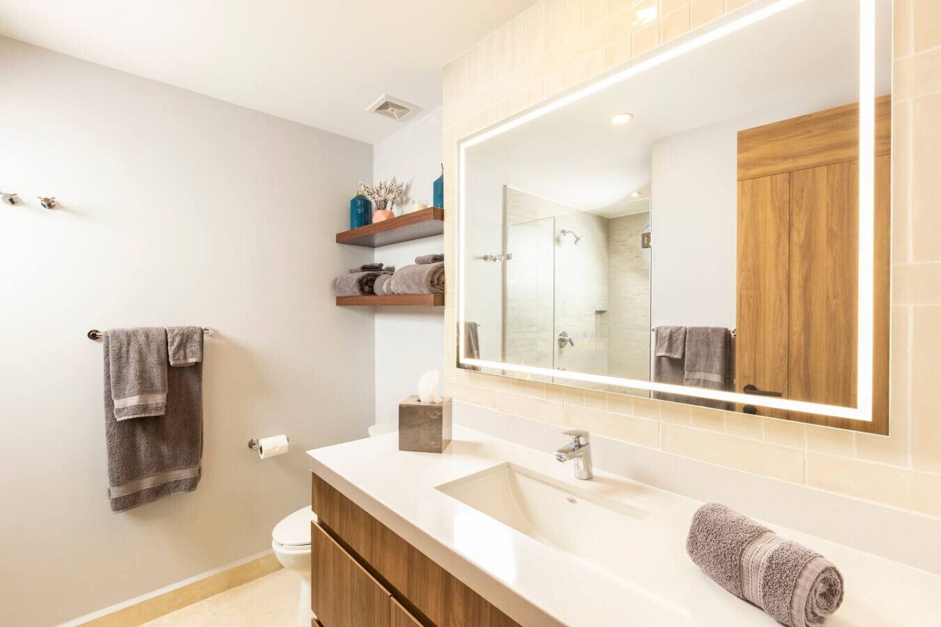 Un baño moderno con un espejo grande, tocador de madera y un inodoro.