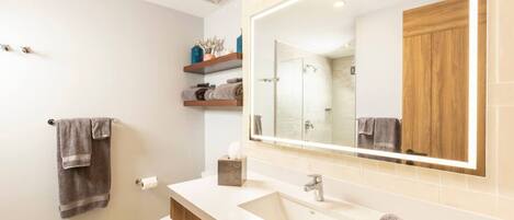 Un baño moderno con un espejo grande, tocador de madera y un inodoro.