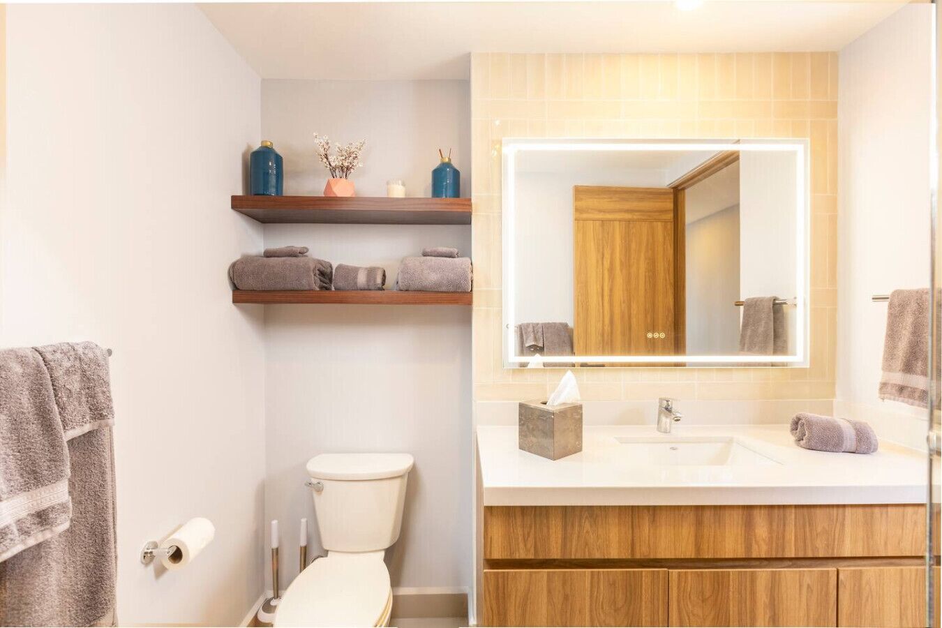A bathroom with a toilet, a sink, a mirror, and a shelf with towels.