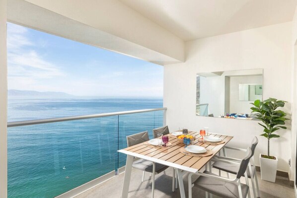 Un balcon avec une table dressée pour le dîner, donnant sur une étendue d’eau.