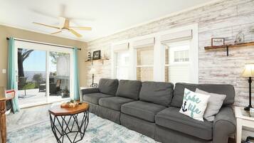 A living room with a gray sofa, a wooden coffee table, and a view through a glass door to an outdoor deck.