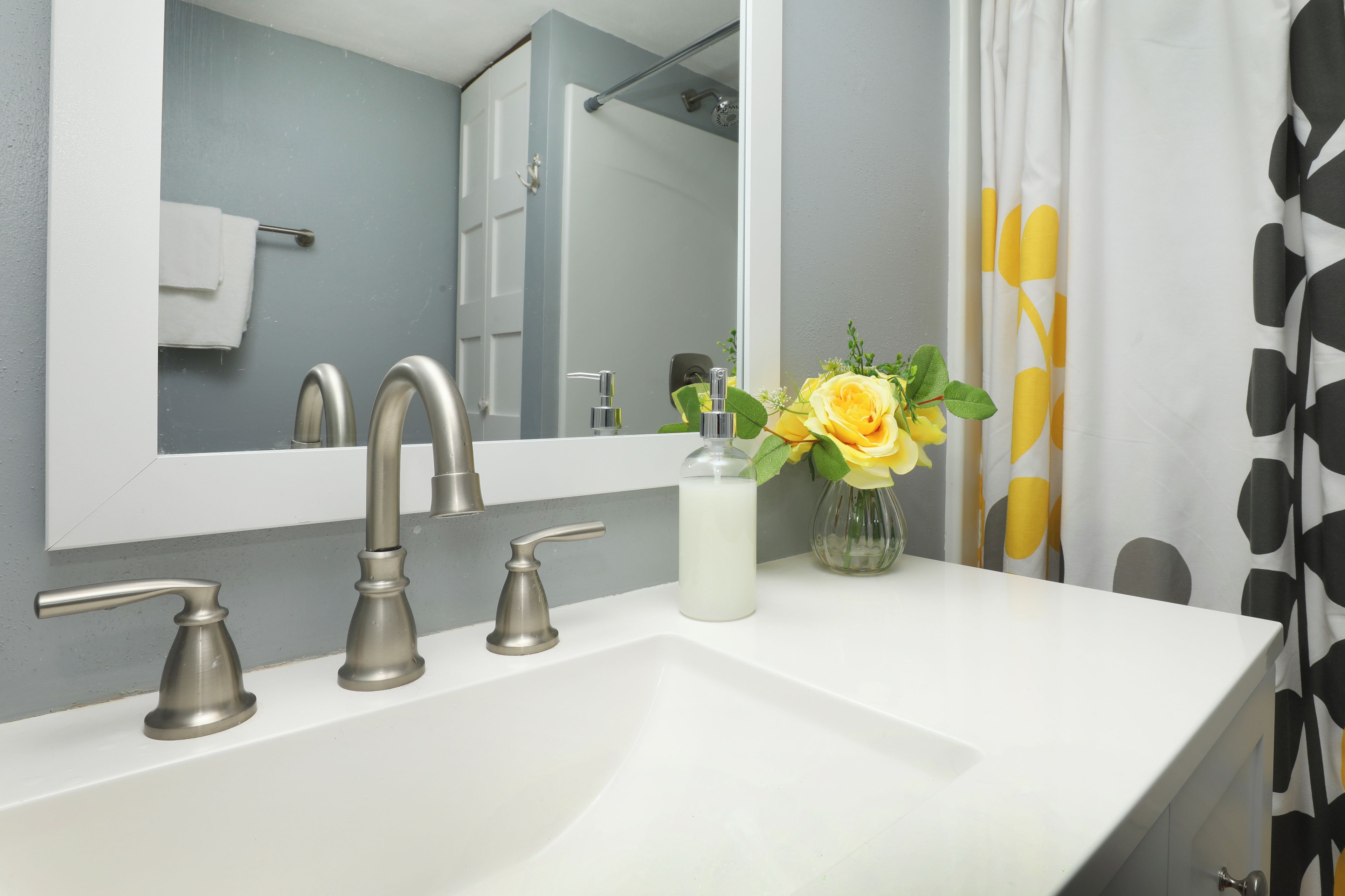 Een badkamer met een witte wastafel, twee kranen, een spiegel en een douche.