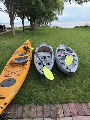 Three kayaks on a grassy area near a body of water.