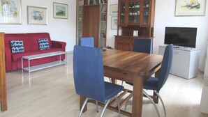 A living room with a wooden dining table, blue chairs, a red sofa, and a television.