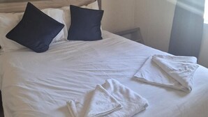 Un letto rifatto con lenzuola bianche e due cuscini scuri.