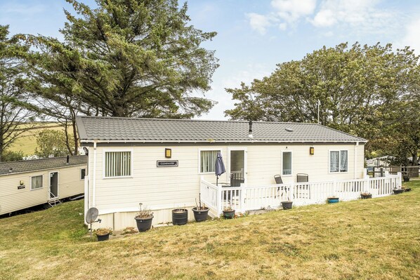Une maison mobile de plain-pied avec un porche, portant l’inscription « CLEARWATER », entourée de pelouse et d’arbres.