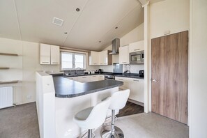 Une cuisine moderne avec des meubles blancs, un îlot central doté de tabourets, un four à micro-ondes et une cuisinière.