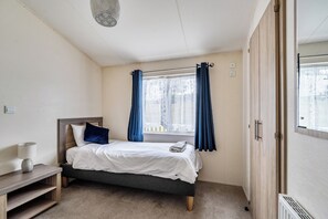 Une chambre à coucher avec un lit, une table de chevet, une fenêtre avec des rideaux et une armoire.