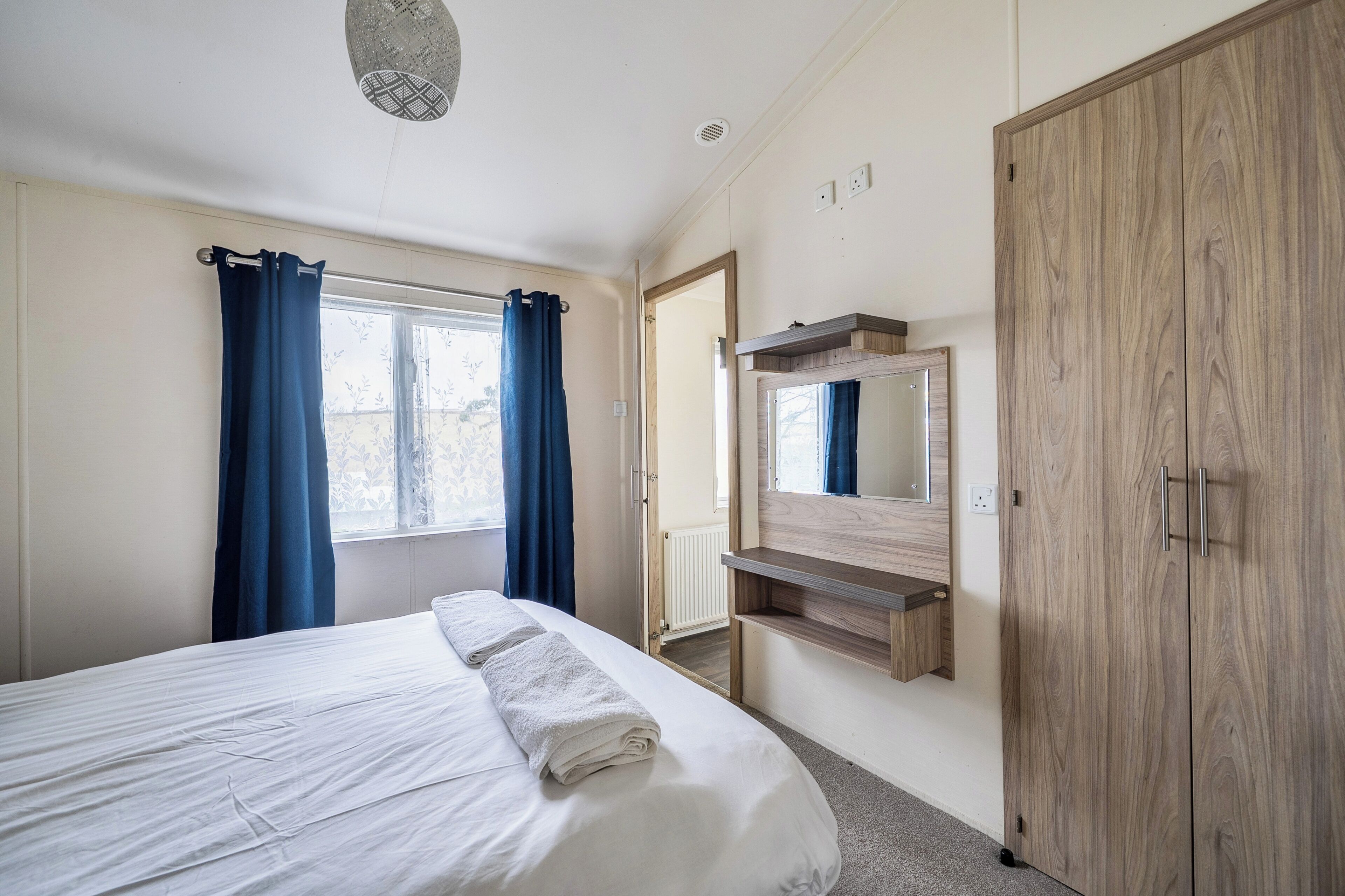 A bedroom with a bed, a wardrobe, a mirror, and a window with curtains.