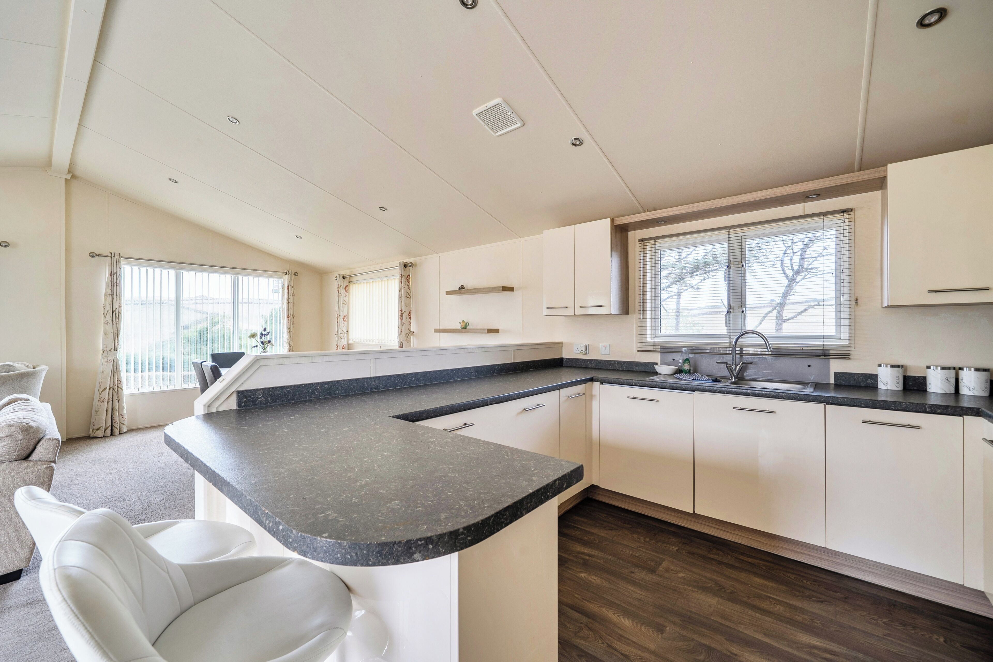A modern kitchen with a central island, white cabinetry, and a window with blinds.