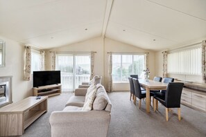A spacious living area with a sofa, TV, dining table, and chairs. - 2 Bed Caravan - Sleeps 6 - Pets - Pool - Parking (Newquay)