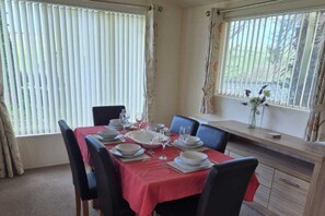 A dining area with a table set for four, chairs, a vase with flowers, and a window with blinds.
