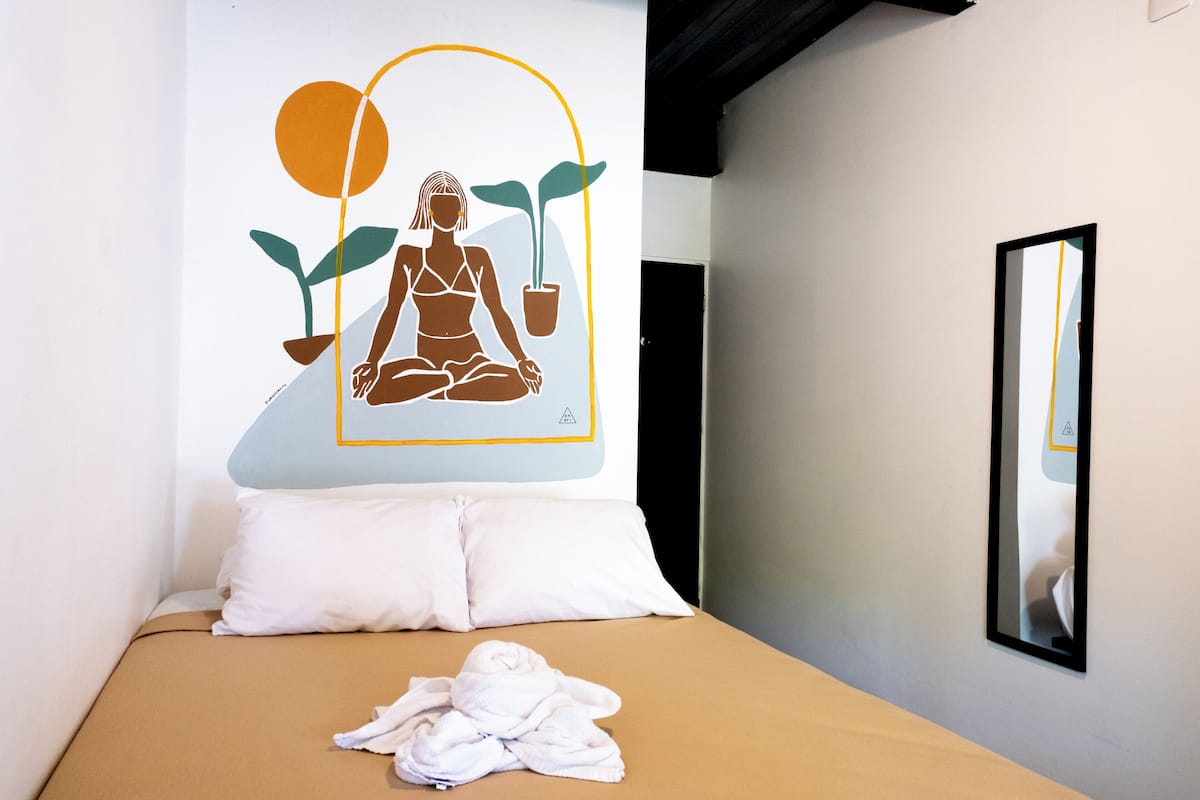 A bed with a tan cover, white pillows, and a towel on the bed.