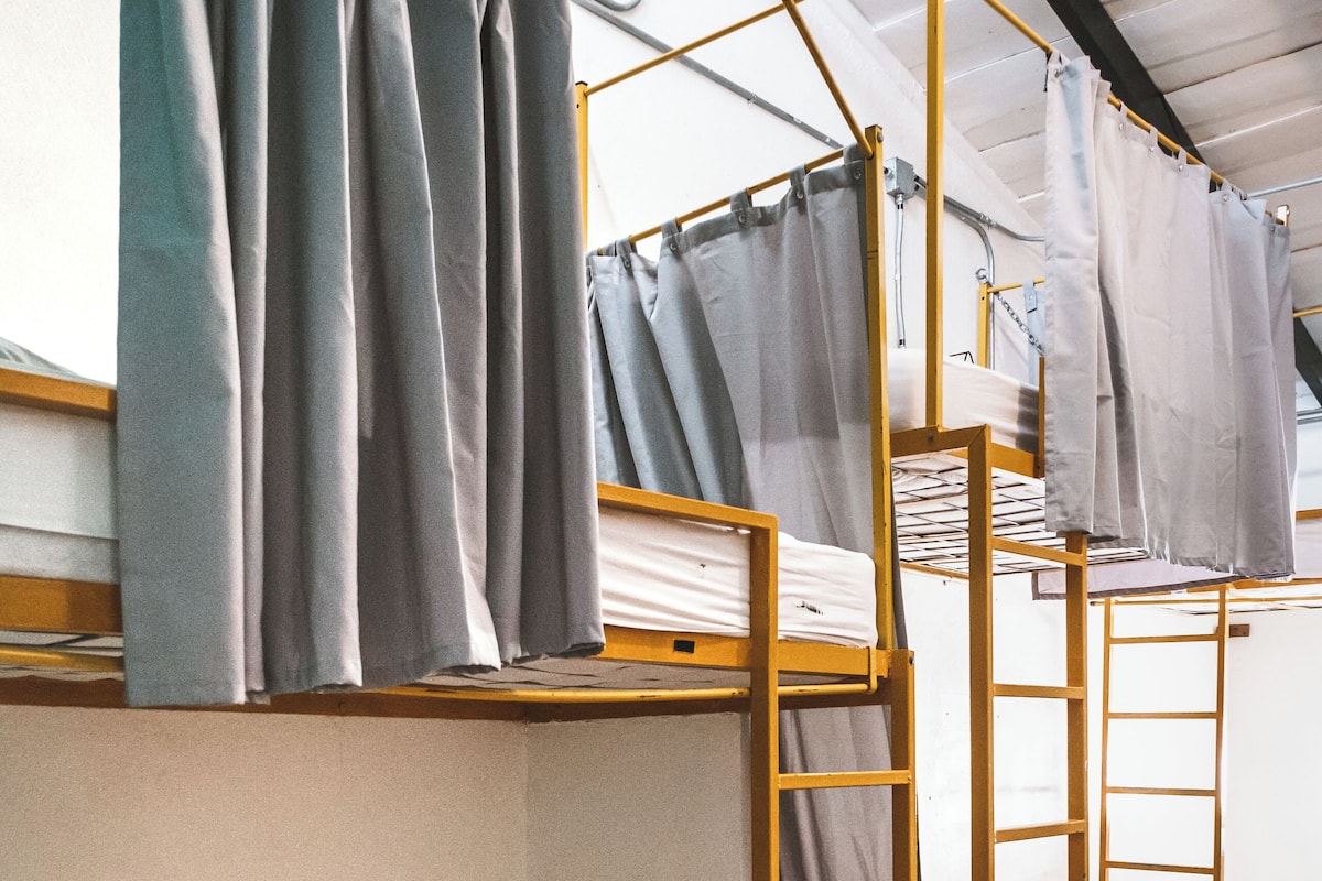 A bunk bed room with a ladder, a window with curtains, and a tiled floor.