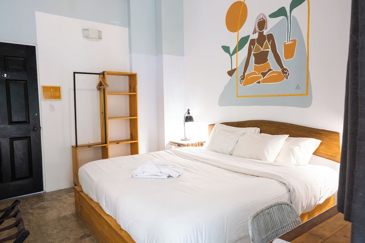 A neatly made bed with white linens, a wooden headboard, and a wall-mounted shelf.