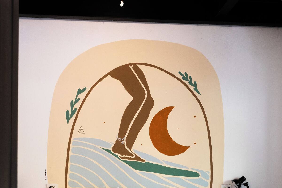 A bed with white bedding, a wall mural of a crescent moon and waves, and a ceiling fan.