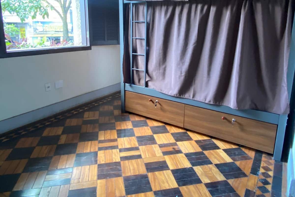 Una stanza con un letto a castello, una finestra con tende e un pavimento di legno a scacchi.