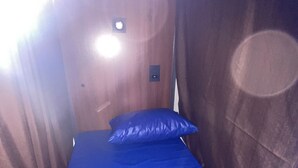 A small, narrow room with a single bed, a nightstand, and a wall-mounted light fixture. - Hostel Das Geraes (Belo Horizonte)