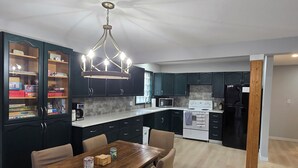 A modern kitchen with dark cabinets, a wooden dining table, and a chandelier.