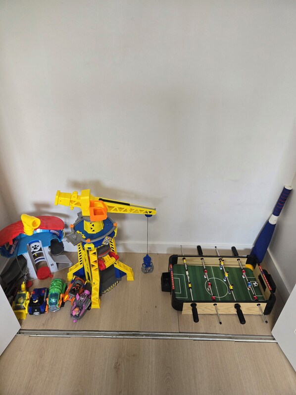 Una habitación con piso de madera, una pequeña cancha de fútbol cubierta y diversos juguetes y equipos de juego.
