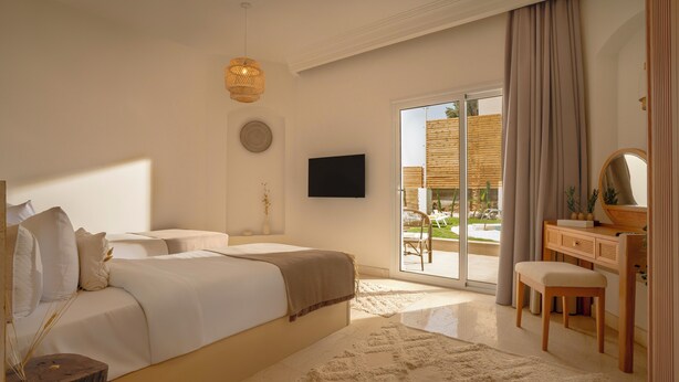 A bedroom with a large bed, a TV, a desk, and a view of the outdoors. - Noya By Dhara Hotels (Giza)