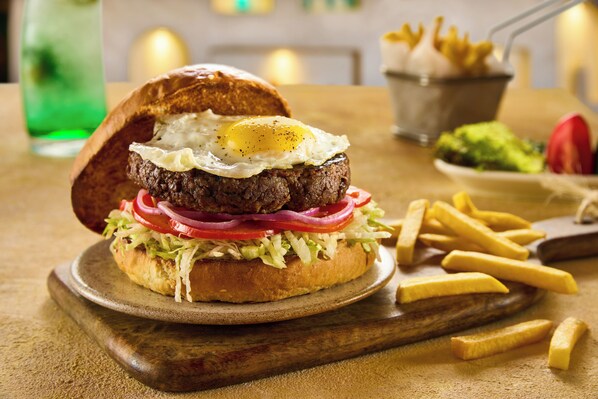 A burger with a fried egg on a bun, surrounded by lettuce, tomato, and red onion, with fries on the side. - Noya By Dhara Hotels (Giza)