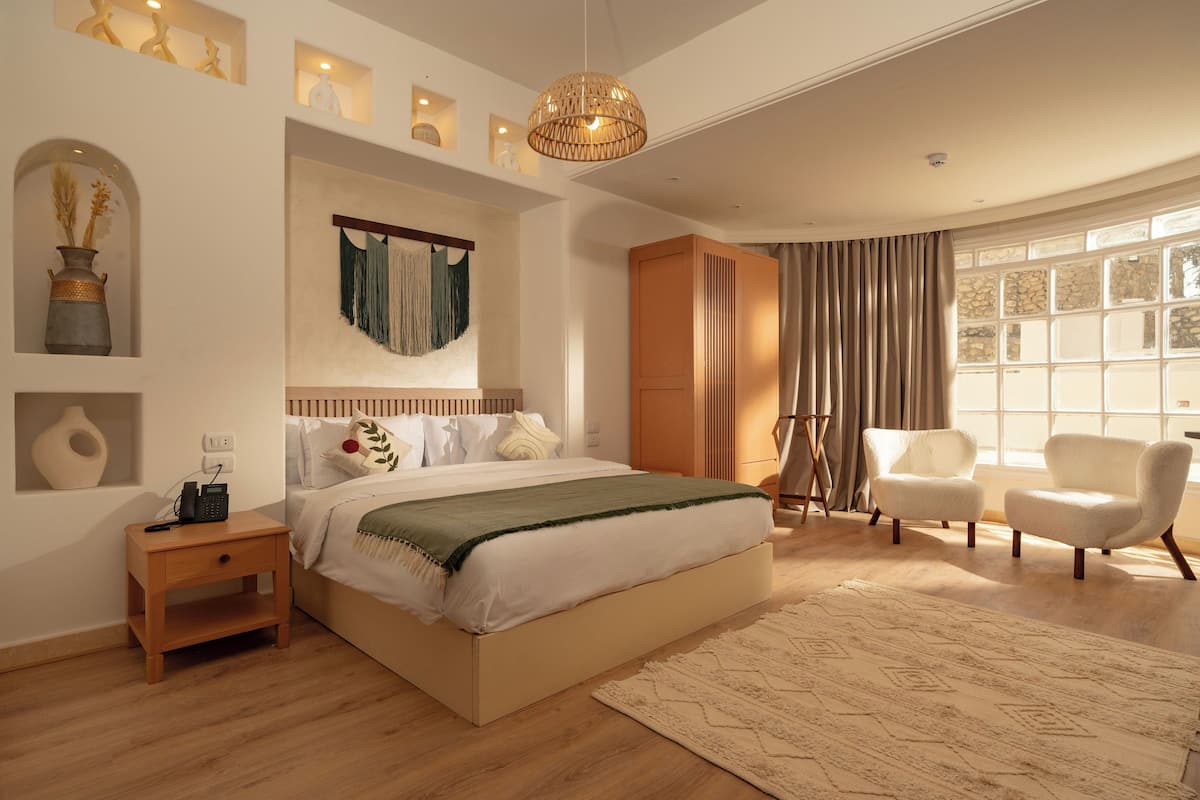 Een ruime slaapkamer met een groot bed, nachtkastje, kast, stoel en een groot raam met gordijnen.
