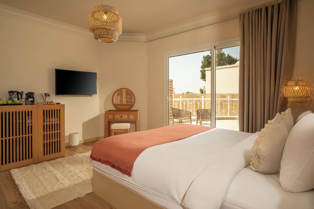 Een slaapkamer met een groot bed, een televisie, een houten kast en een balkon met stoelen.